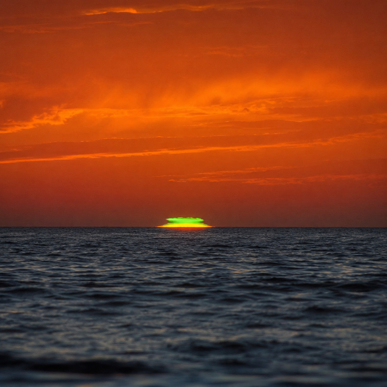 A vivid green flash at the upper edge of the setting Sun over the ocean
